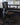 A dark gray ergonomic office chair with a mesh back and five-wheel base, positioned in front of a desk with dual computer monitors in an office setting.