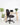A black fabric office chair with a five-star wheeled base, positioned in front of a light wood desk with a laptop and flowers, set against a white wall and light floor with potted plants.