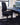 A black ergonomic office chair with a high back and five-wheel base, positioned in front of a dark desk in a home office setting.